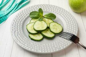 dieta concepto. diapositivas de Fresco Pepino en un plato y cinta centímetro en un blanco mesa. foto