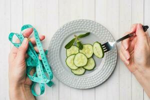 dieta concepto. diapositivas de Fresco Pepino en un plato y cinta centímetro en el palmas en un blanco mesa. foto