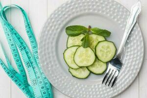 dieta concepto. diapositivas de Fresco Pepino en un plato y cinta centímetro en un blanco mesa. foto