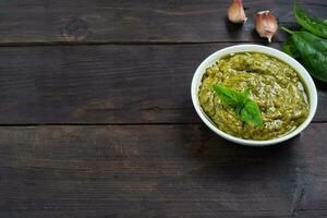 Pesto sauce in a plate and fresh basil leaves with garlic. dark wooden background, copy space. photo