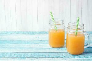 Orange juice in glass jars and fresh oranges on a blue background. photo