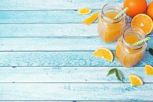 Orange juice in glass jars and fresh oranges on a blue background. photo