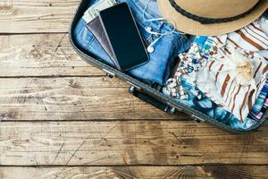 Travel preparations concept with suitcase, clothes and accessories on an old wooden table. Top view Copy space photo
