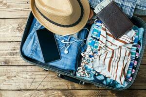 Travel preparations concept with suitcase, clothes and accessories on an old wooden table. Top view Copy space photo