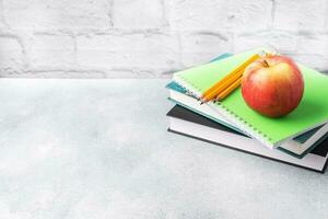 A fresh red apple on a stack of books and notebooks. The concept of a school breakfast snack. Copy space, photo