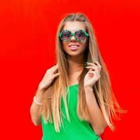 Cheerful portrait of pretty woman smiling in sunglasses near a bright red wall photo