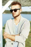 hermoso hombre con un barba en Gafas de sol y chaqueta en el playa foto