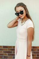 Pretty woman with sunglasses in a pink dress near the green wall photo