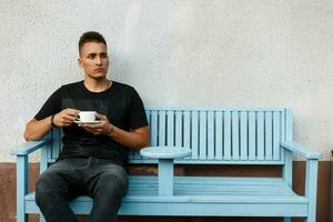 hermoso joven hombre con café en un banco foto