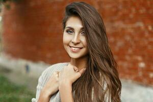 hermosa niña sonriente con un dulce sonrisa en un gris suéter cerca rojo ladrillo pared foto