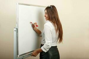 Beautiful sexy woman standing near whiteboard and writing with a red marker. photo