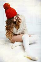 Beautiful fashionable American girl in knitted warm clothes on a background of lights. Woman sitting on white wooden floor photo