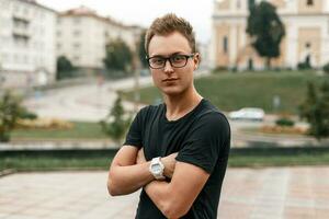 Young handsome guy in black glasses and a black t-shirt on the background of the city photo