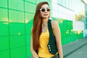 Beautiful young girl in fashionable jeans clothes near a green wall photo