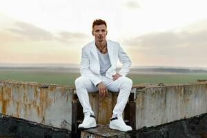 Young handsome man in a stylish white clothes sitting on the roof. photo