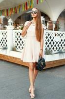 Stylish woman in a long pink dress with handbag posing near the white vintage fence photo