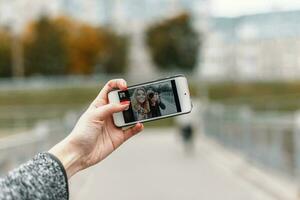 Beautiful girl with friend photographer to take photos on phone