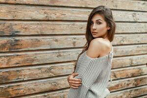 Sexy beautiful woman in a gray sweater standing near the wooden wall photo