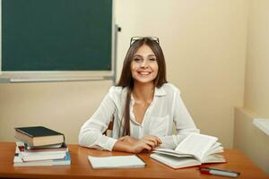Beautiful happy teacher sitting at the desk with books and writes in a notebook. photo