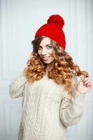 Fashionable young girl with curly hair in a red knitted hat and vintage sweater. photo