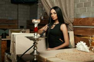 Beautiful girl sitting on a sofa and smokes a hookah. photo