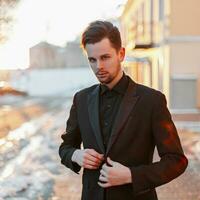 Handsome young businessman in black suit at sunset photo