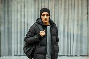 Handsome man in a black jacket and a fashion warm hat posing near the windows. photo