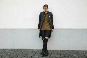 Handsome young man with glasses in a stylish jacket and torn black jeans. photo