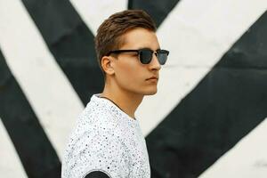 joven hermoso chico con un peinado y Gafas de sol en un antecedentes de negro y blanco rayas. foto