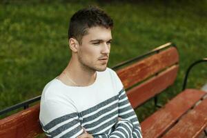 Handsome guy with a beard in a stylish pullover sits and resting on the bench. photo