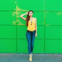 elegante hermosa joven mujer en un amarillo camiseta, pantalones y amarillo Zapatos posando cerca un brillante verde pared foto