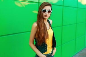 elegante hermosa modelo niña en un brillante amarillo camisa y pantalones ropa posando cerca un verde metal pared. foto