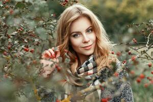 hermosa mujer en Clásico de punto bufanda posando cerca un árbol con bayas. otoño día. foto