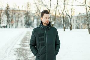 hermoso hombre con un barba y pelo en invierno chaqueta caminando en un Nevado parque foto