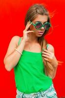 Pretty woman in fashionable round sunglasses near the red wall photo