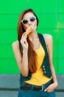 Young stylish girl eating a delicious ice cream near the green wall. photo