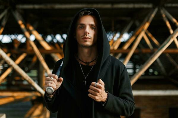 Stylish handsome man in a black robe with a hood holds a bat.
