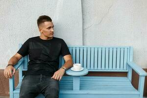 Handsome sad man alone on a bench and drink coffee. photo