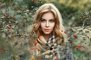 Beautiful blonde girl with a knitted scarf in autumn day near a tree. photo