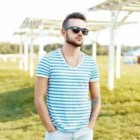 Handsome man in a stylish shirt and sunglasses resting on the beach. photo