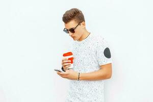 Handsome guy with a mobile phone and a cup of coffee against a white wall photo