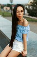 hermosa asiático mujer en un azul verano blusa con blanco pantalones cortos en un ciudad antecedentes en un verano día. foto