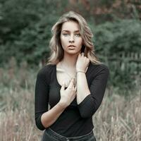 hermosa joven rubia niña en un negro camiseta en un campo cerca arboles foto