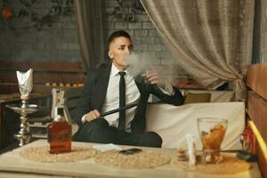 Young rich man in an elegant suit has a rest in a bar and smokes a hookah. photo