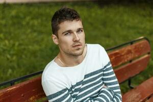 Man in a stylish pullover sitting on a bench. photo