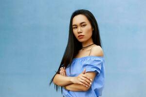 Beautiful brunette asian girl with long hair folded his hand for hand on a blue background. photo