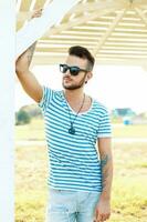 Handsome hipster man in sunglasses with a tattoo on the beach on a sunny day photo