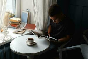 hermosa moderno hombre descanso en un restaurante, leyendo un libro y Bebiendo café. foto