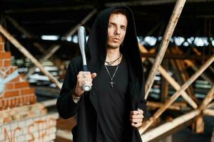 Trendy man with a hood holds a bat on the background of the old buildings photo