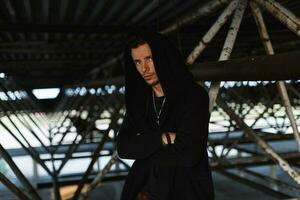 Handsome fashionable man in a stylish robes with a hood near metal structures photo